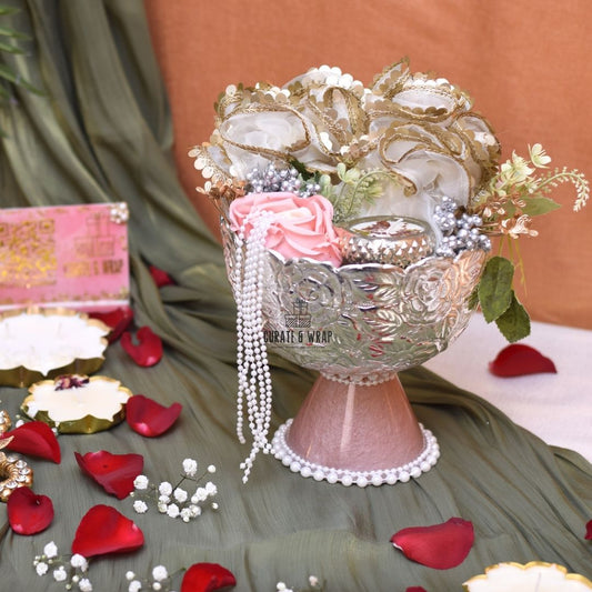 Decorative glass bowl with floral and pearl embellishments on a tablecloth with red rose petals.