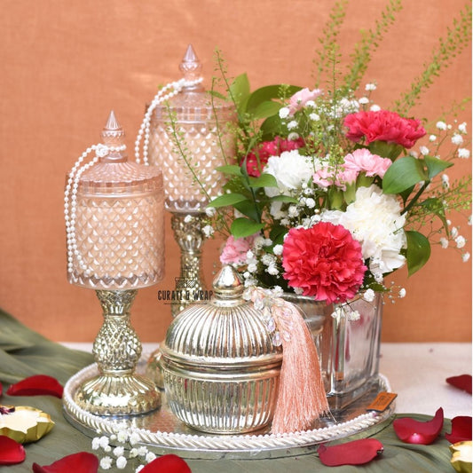 Decorative table setting with floral arrangement and ornate containers on a peach-colored background