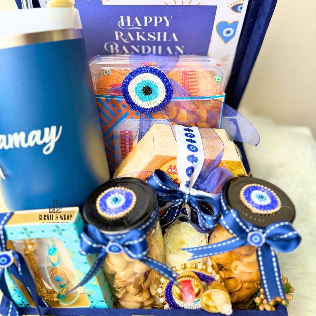 Gift basket with snacks and a blue tumbler labeled 'may' for Raksha Bandhan celebration.
