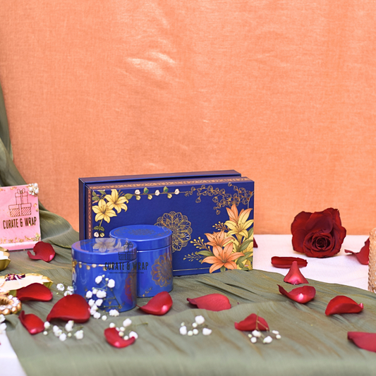 Decorative blue box with floral design on a green surface with red rose petals and a pink card.