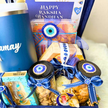Gift basket with snacks and a blue tumbler labeled 'may' for Raksha Bandhan celebration.