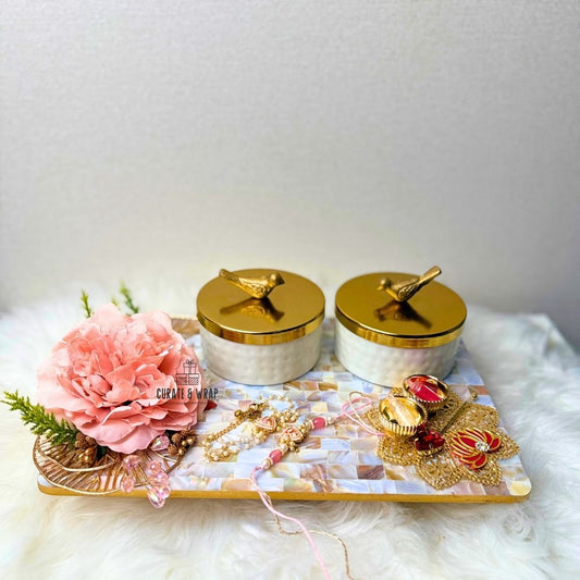 Decorative tray with jewelry, pink flowers, and gold containers on a white surface.