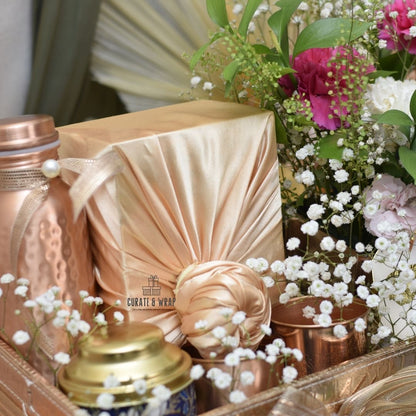 Decorative setup with copper containers, pink fabric, and flowers on a reflective surface.