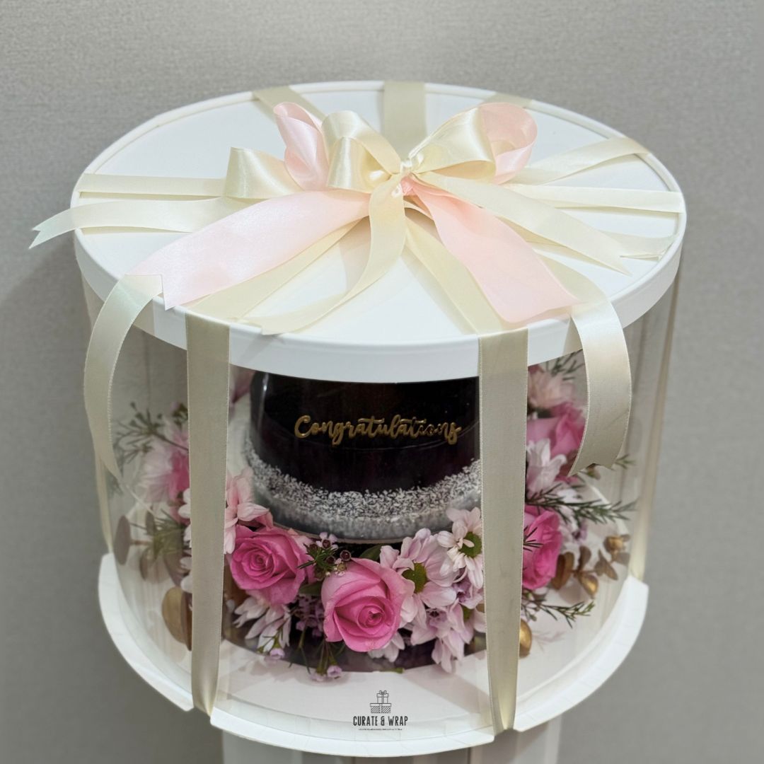Luxury gift hamper with half kg cake and fresh pink flowers in a round box by Curate and Wrap, ideal for all occasions.