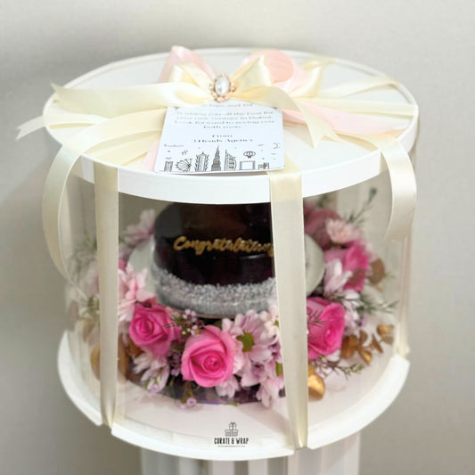 Luxury gift hamper with half kg cake and fresh pink flowers in a round box by Curate and Wrap, ideal for all occasions.