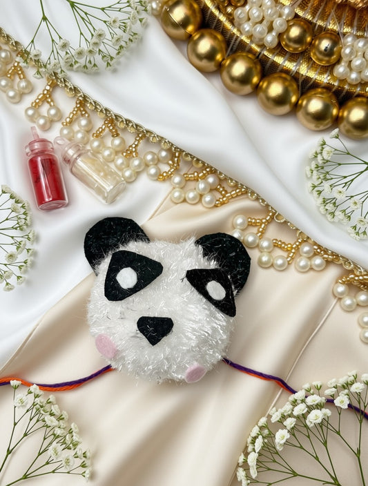 A plush panda face accessory with black and white fur-like texture, pink cheeks, and small multicolored ear strings, styled on cream satin fabric with pearl strands, gold beads, white baby's breath flowers, and two small pink bottles.