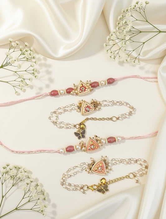 Four delicate rakhi-style bracelets arranged on a cream satin background with white baby's breath flowers. The bracelets feature pink cords, gold-tone chains, small pearl-like beads, and central motifs including a pink-and-gold heart with a crown, a butterfly, and a small bell.