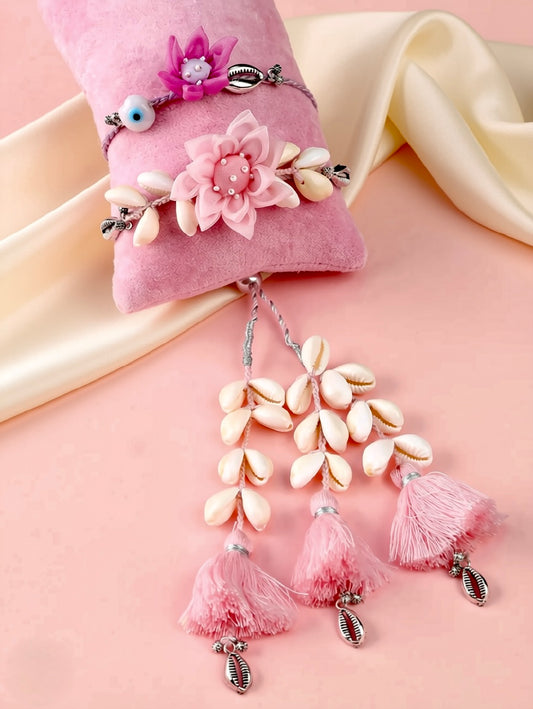 A pink fabric jewelry stand holding a pink bracelet decorated with a flower, beads, and a blue evil eye charm, with matching dangling tassel earrings below on a pink and cream satin background.