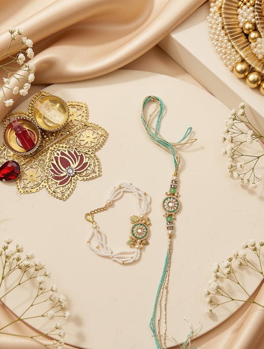 A styled flat-lay of jewelry on a cream-colored surface with draped satin fabric and baby's breath flowers. The main products appear to be a gold-toned ornate brooch with red and cream enamel details, a white beaded bracelet with a gold floral charm, and a long turquoise and gold tassel necklace or rakhi-style piece with green stone accents.